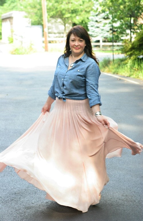 woman in a denim shirt tied at the waist paired with a blush pink maxi length ballerina skirt from ann taylor