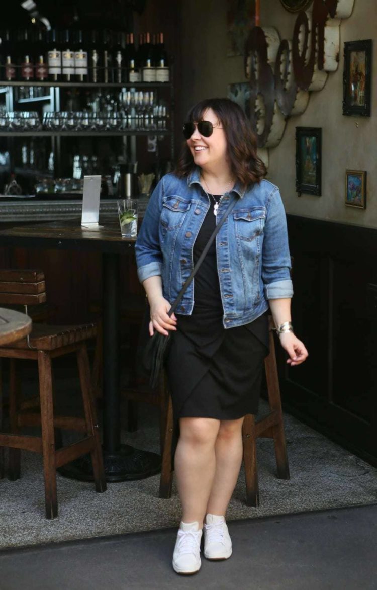 how to wear black in summer featuring Alison Gary of Wardrobe Oxygen in a black knit knee length dress with a denim jacket, black crossbody bag, and white sneakers