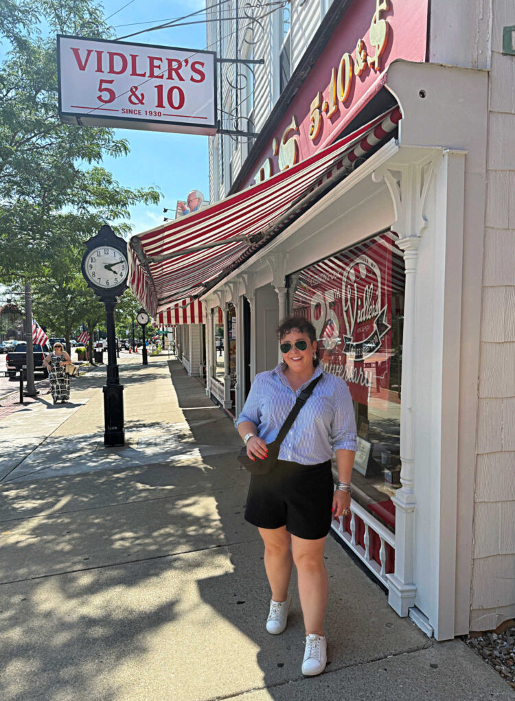 woman in a blue and white striped shirt and black ponte shorts standing in front of Vidler's 5 & 10 in East Aurora, New York