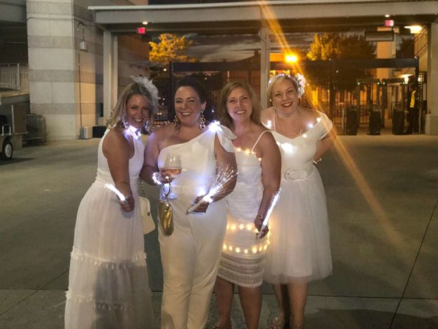four women over 40 dressed in white cocktail dresses and jumpsuits with twinkle lights woven into their dresses at Diner en Blanc DC