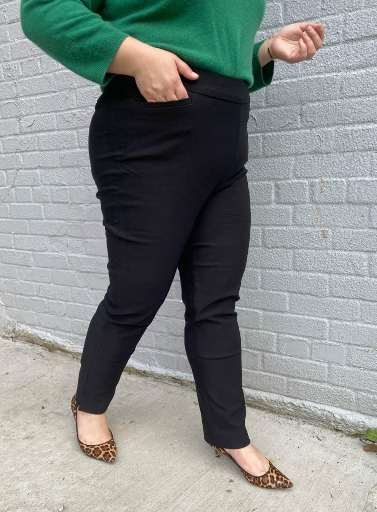 She is wearing a green sweater tucked into black Chico's Bridgitte slim ankle pants.