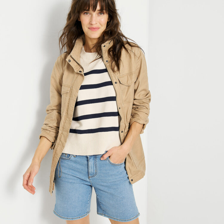 Lands' End Spring is So Good 1 Lands' End model in a tan twill jacket, cream sweater with navy stripes, and knee-length faded denim shorts