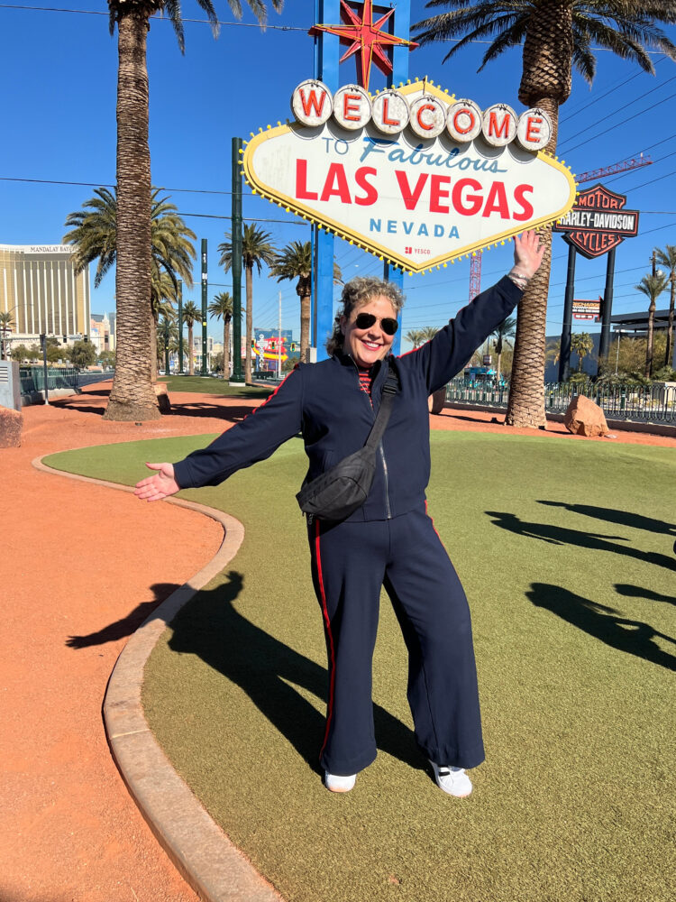 Alison Gary in a navy ponte track suit standing at the Welcome to Las vegas sign | The Weekend After January 28th
