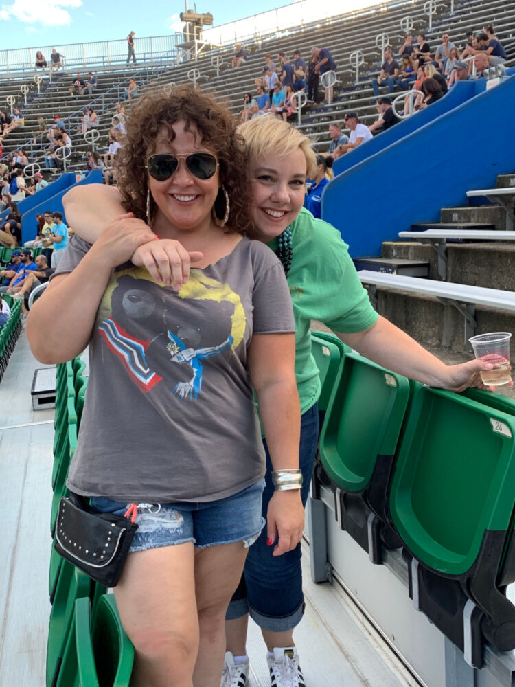 Two women over 40 at an outdoor concert wearing denim shorts and My Morning Jacket band t-shirts